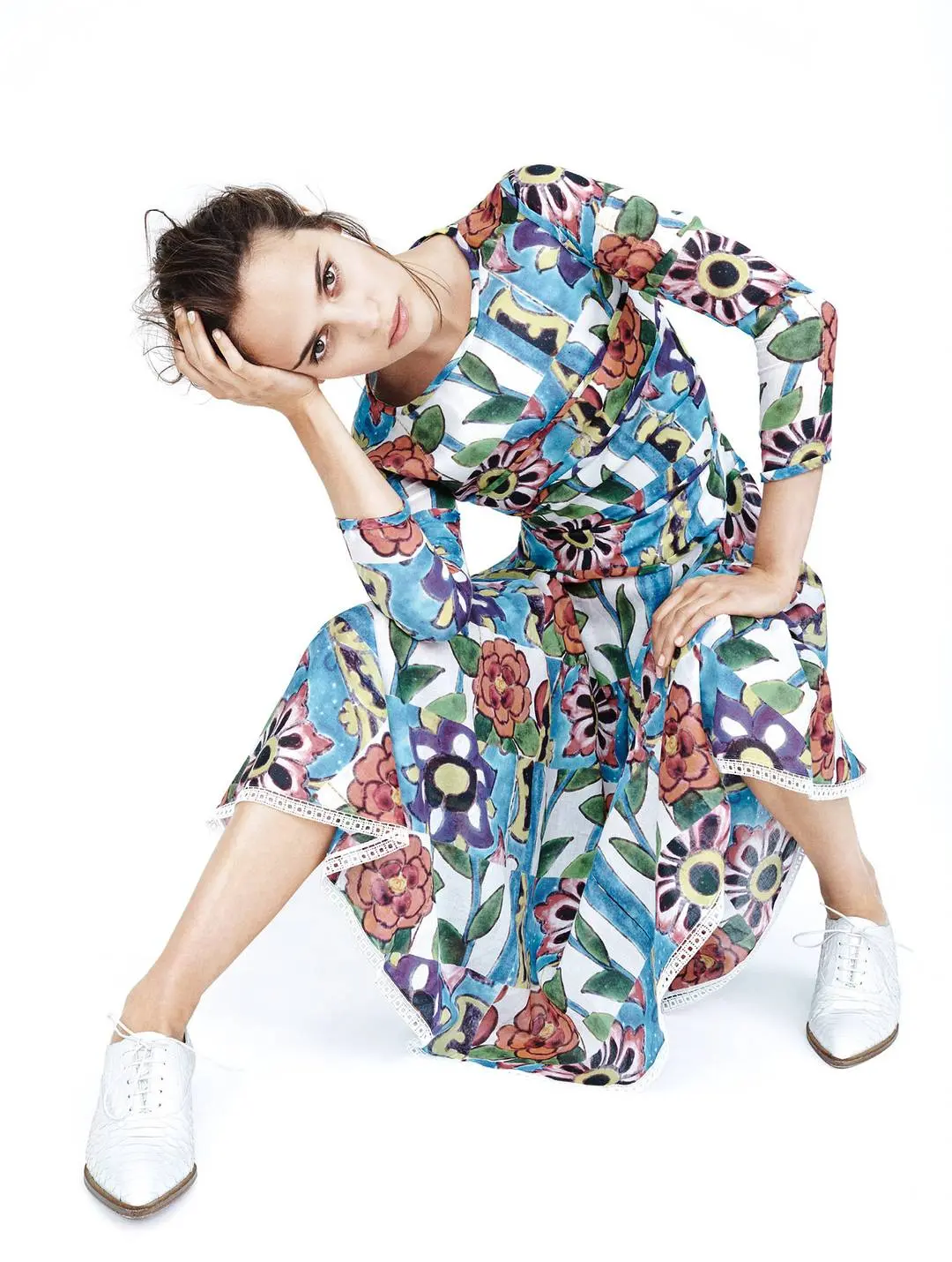 Alicia Vikander posing in a white suit, black dress, and floral gowns with a thigh tattoo