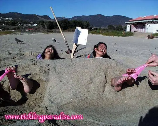 Asian women tickling feet and toes with a pink feather while buried in the sand at the beach