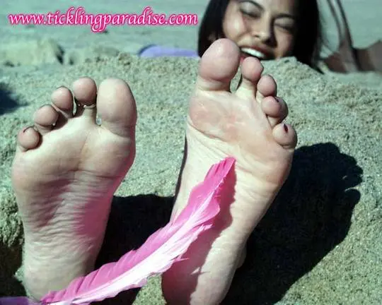 Asian women tickling feet and toes with a pink feather while buried in the sand at the beach
