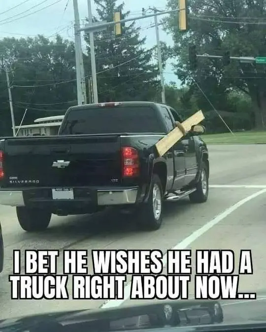 A funny meme of a black Chevrolet Silverado with a long piece of lumber sticking out of the passenger window.
