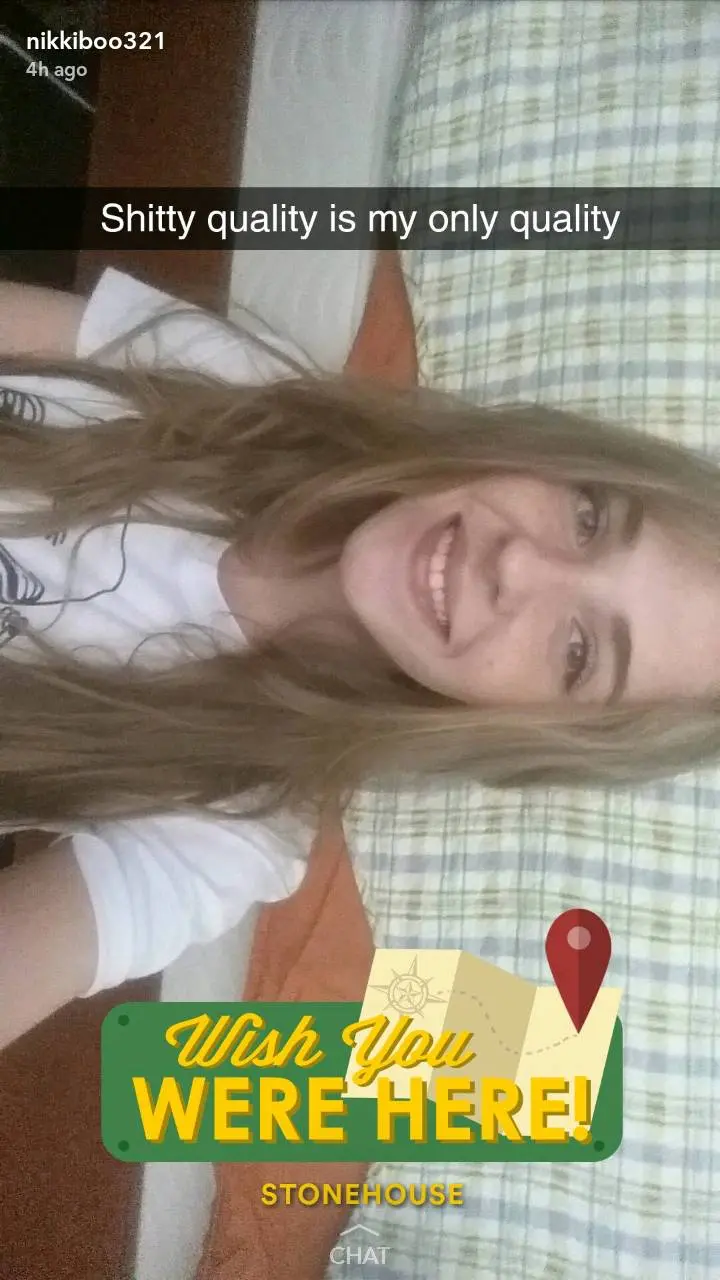 Slim blonde woman in a white t-shirt smiling and cuddling with her white cat in a selfie.