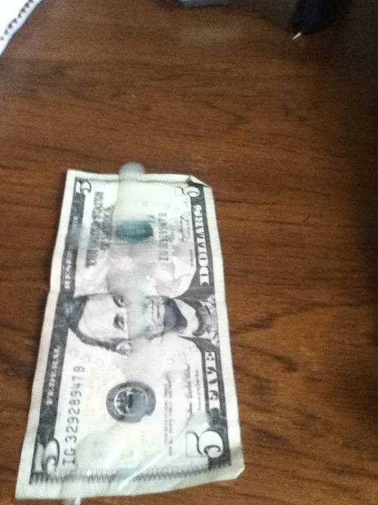Cum on money, a close-up of a five-dollar bill covered in a translucent white substance on a wooden surface.