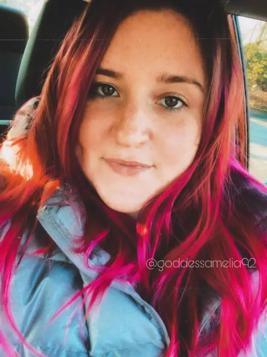 Findom mistress Goddess Amelia with long red and pink hair wearing a grey puffer jacket in a car selfie