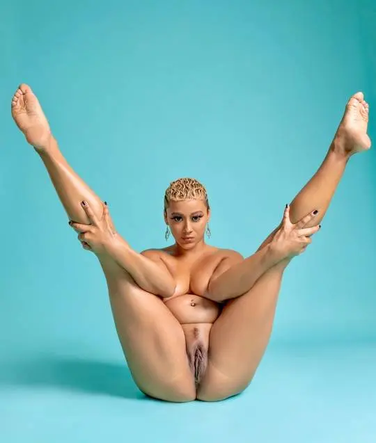 Curvy mixed woman with blonde finger waves posing nude in a flexible split, showing her pussy.