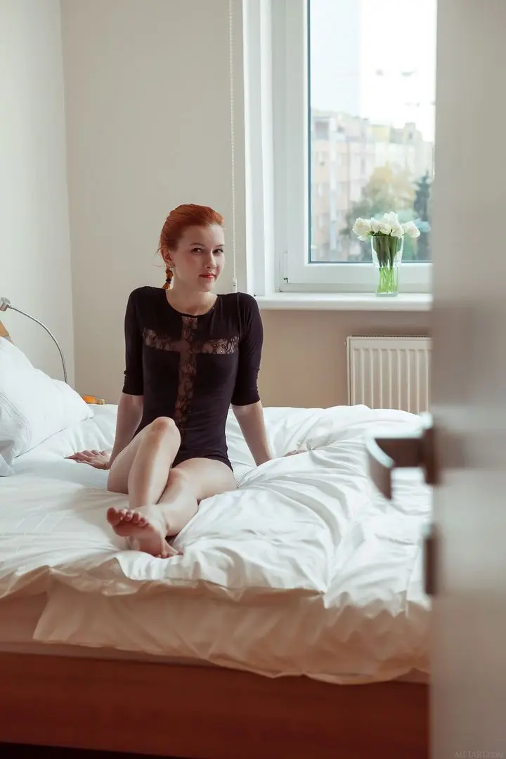 Ambre, a slim redhead in a black lace bodysuit, presenting her beef flaps on a bed