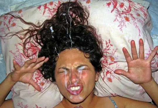 Slim tanned brunette with curly hair lying down with a cum face and an annoyed expression.