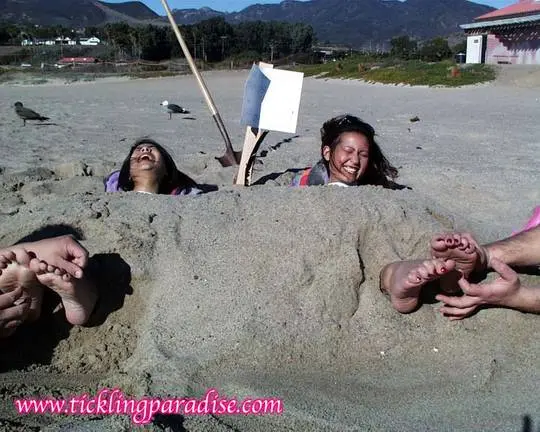Asian women tickling feet and toes with a pink feather while buried in the sand at the beach