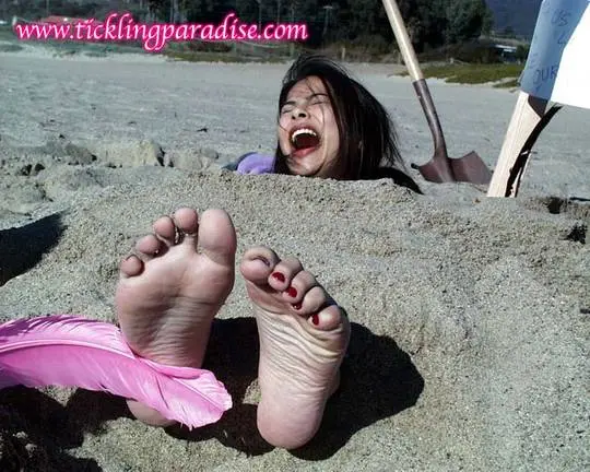 Asian women tickling feet and toes with a pink feather while buried in the sand at the beach
