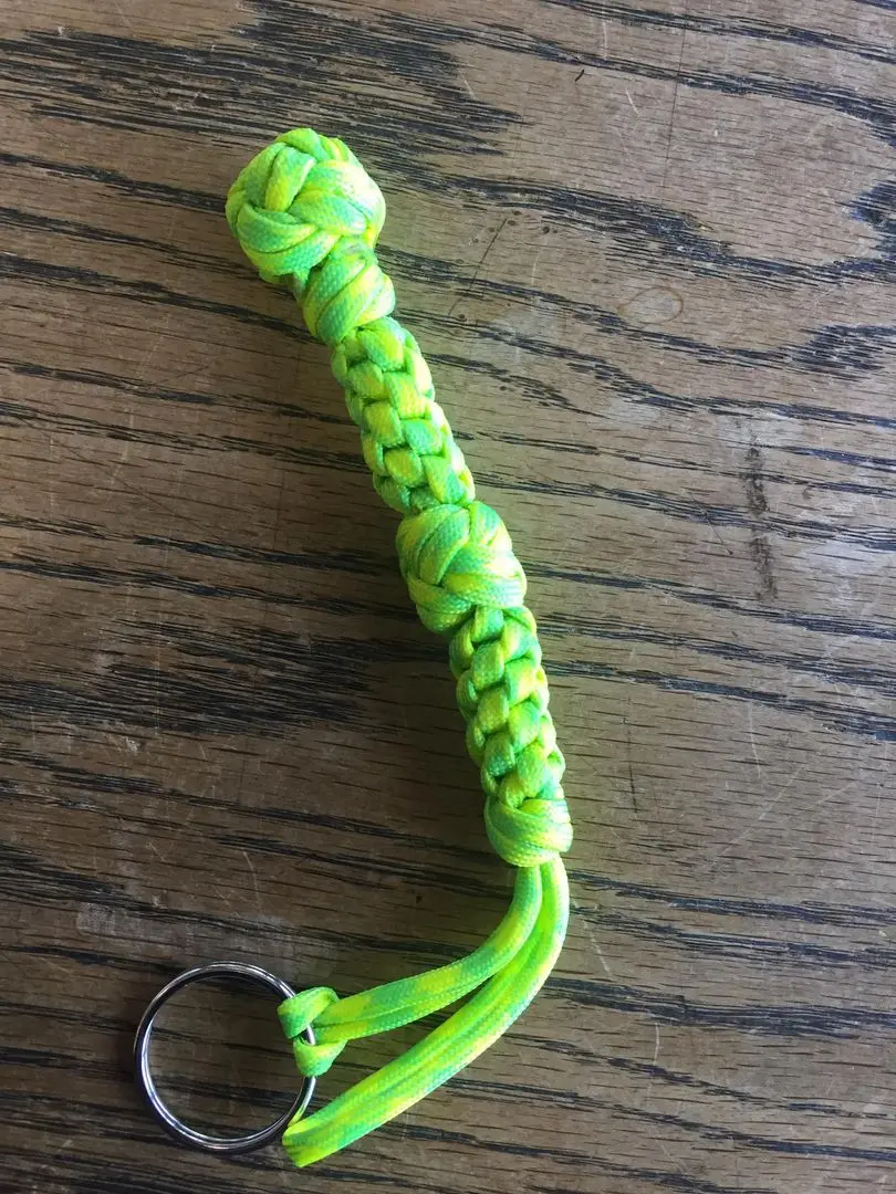 Close-up of a neon yellow and green braided paracord keychain on a dark wooden surface.