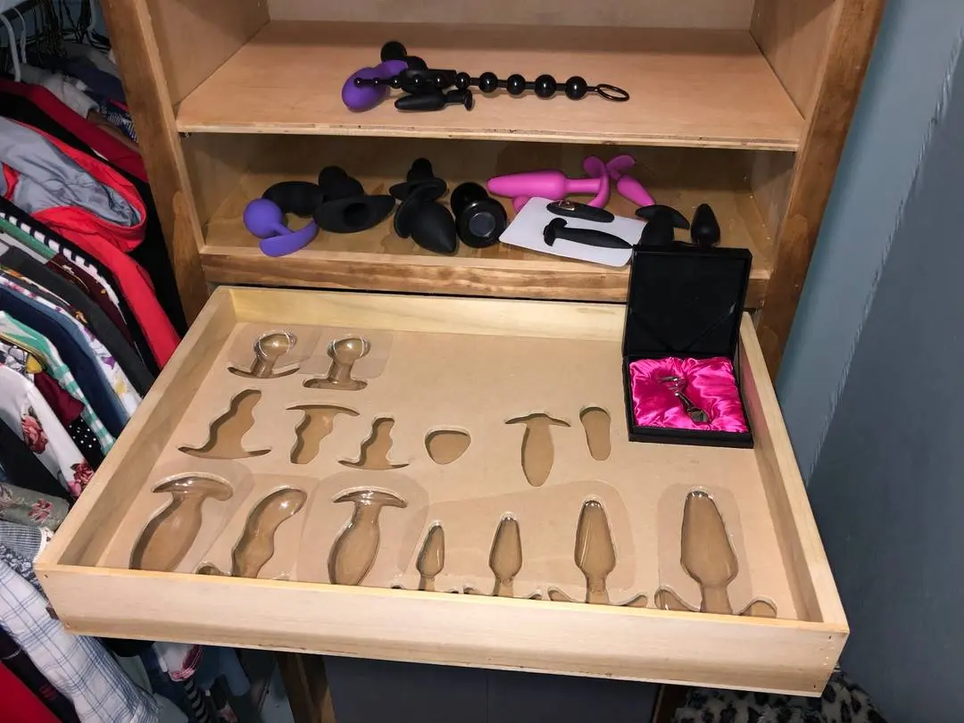 Sex toys including dildos, vibrators, and anal beads organized in a wooden dresser drawer