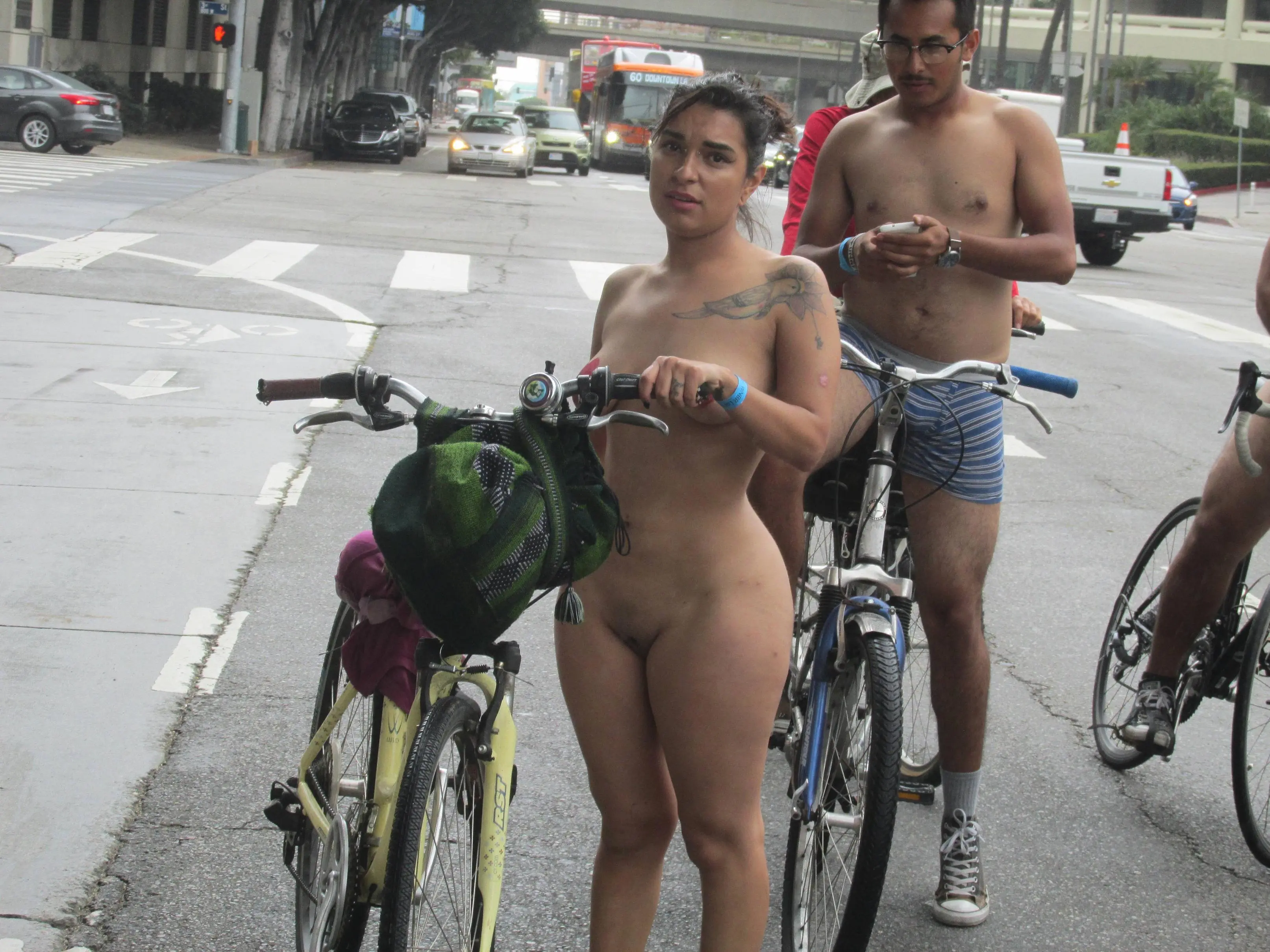 Thick latina with heart pasties and tattoos riding a bicycle at WNBR SF with an interracial group