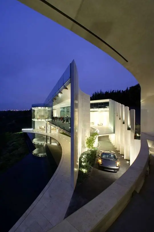 Ultra modern mansion with glass walls and a silver BMW convertible sports car in the driveway at dusk