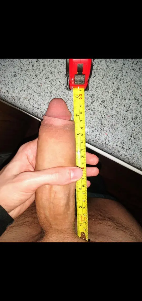 Slim white man taking a pelfie while measuring his 8 inch uncut erection with a yellow tape measure.