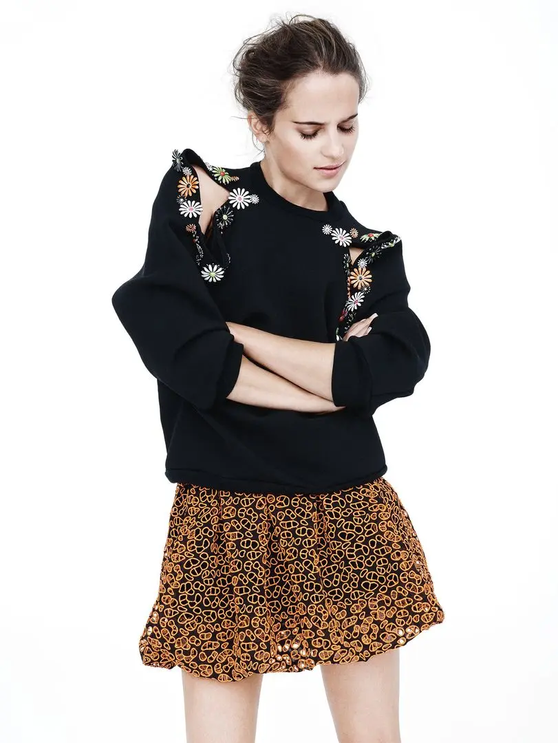 Alicia Vikander posing in a white suit, black dress, and floral gowns with a thigh tattoo