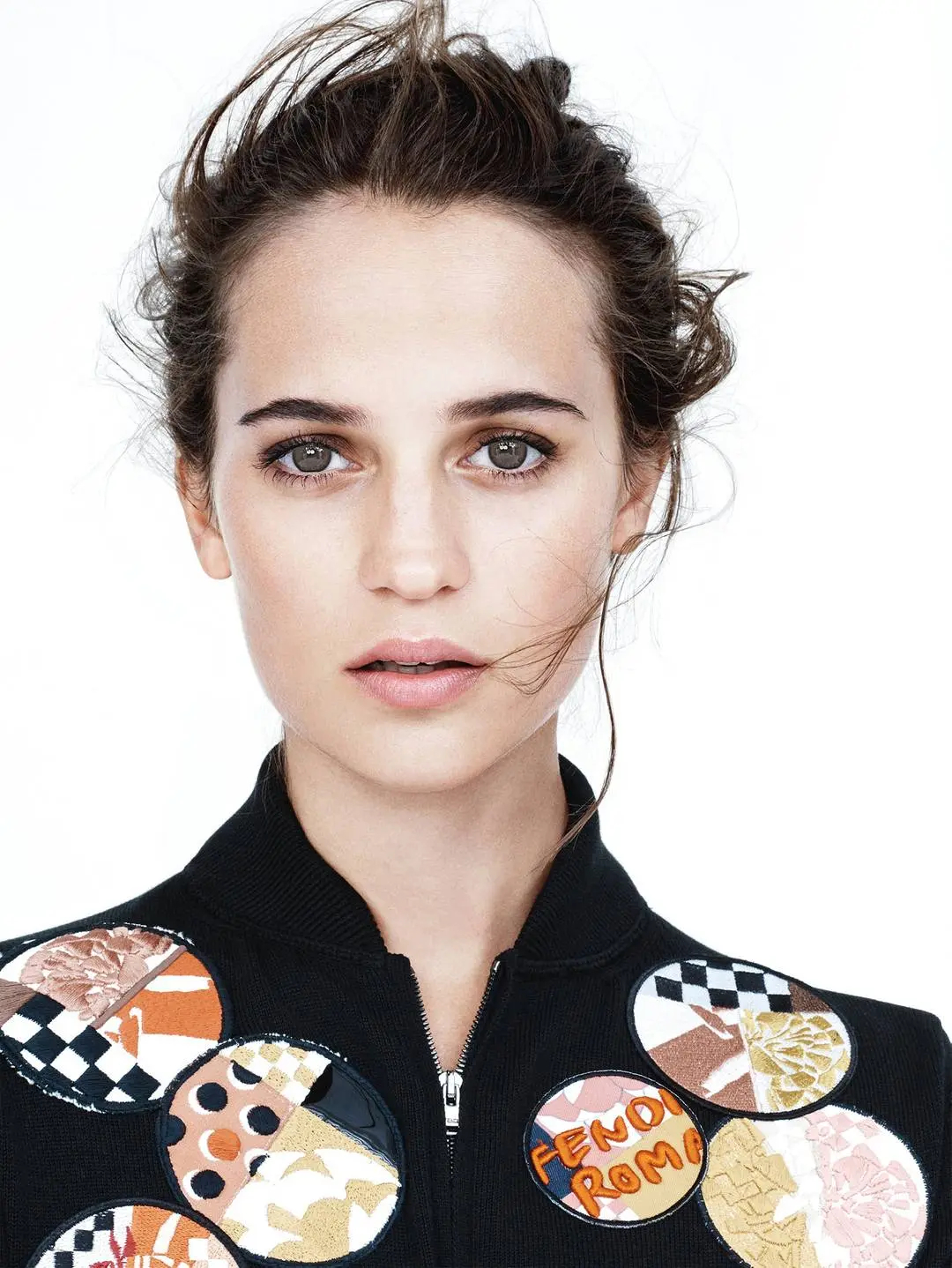 Alicia Vikander posing in a white suit, black dress, and floral gowns with a thigh tattoo