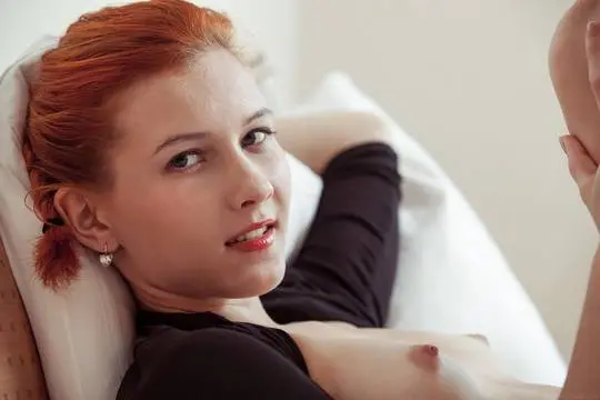 Ambre, a slim redhead in a black lace bodysuit, presenting her beef flaps on a bed