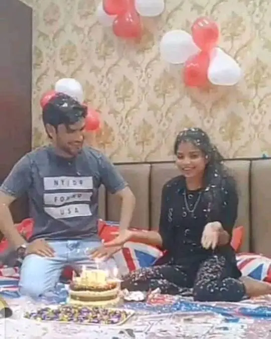 Desi couple celebrating a birthday on a bed with a cake and balloons