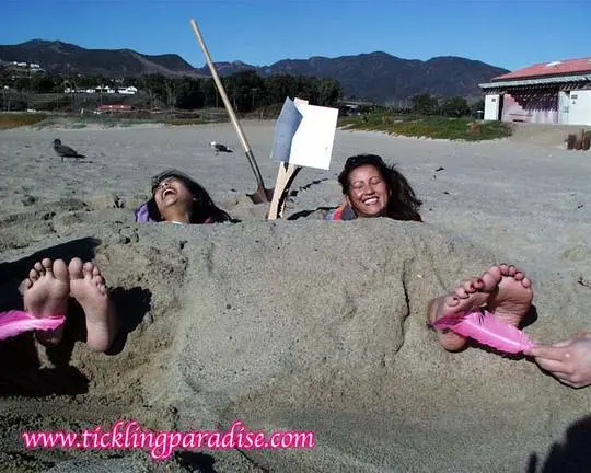 Asian women tickling feet and toes with a pink feather while buried in the sand at the beach