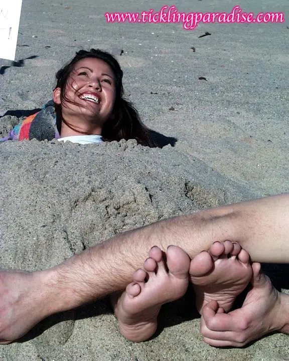 Asian women tickling feet and toes with a pink feather while buried in the sand at the beach