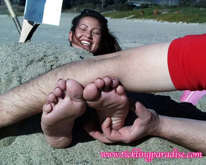 Asian women tickling feet and toes with a pink feather while buried in the sand at the beach