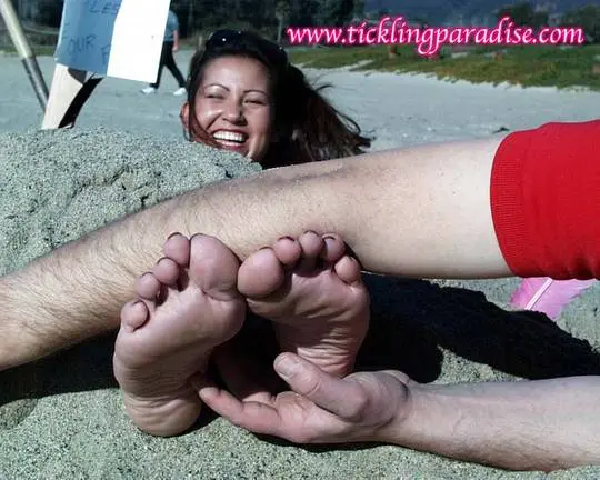 Asian women tickling feet and toes with a pink feather while buried in the sand at the beach