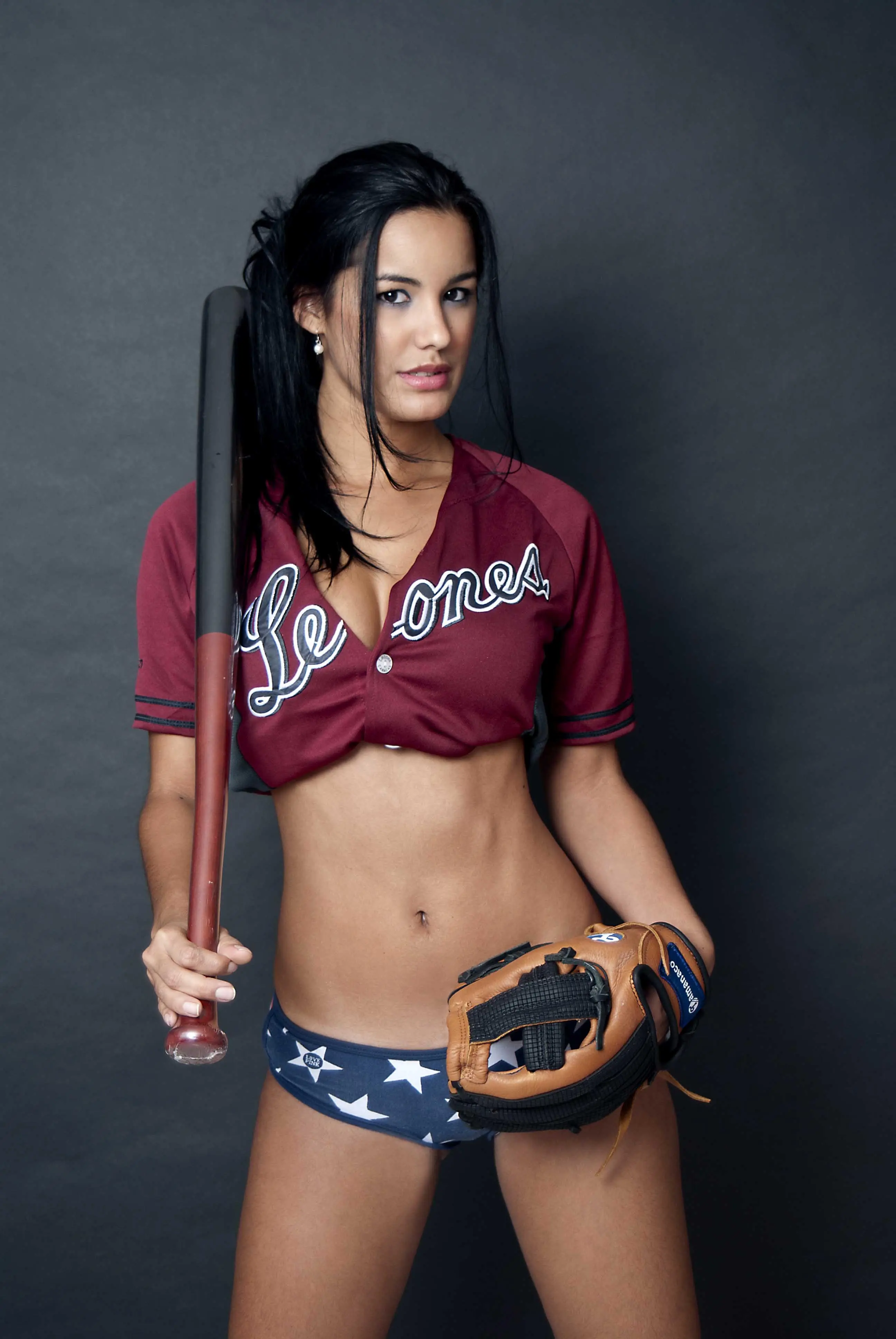 Edmar Leal posing in a baseball jersey, bra, and panties with a bat and glove in a studio