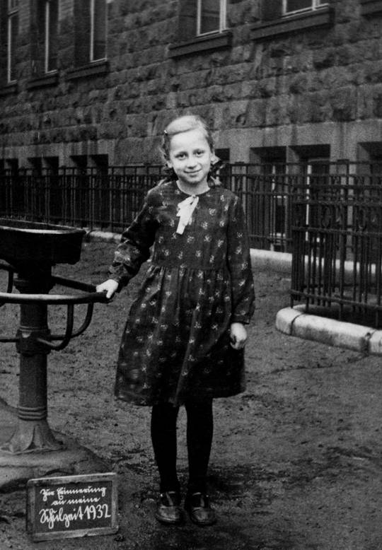German girl (2 of 2), 1932. From a random box of old photos I came across. Can anyone read the caption on the sign near her feet?
