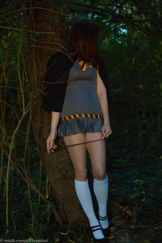 Hermione cosplay woman in a grey skirt and white thigh-high socks posing in a forest, showing her backside