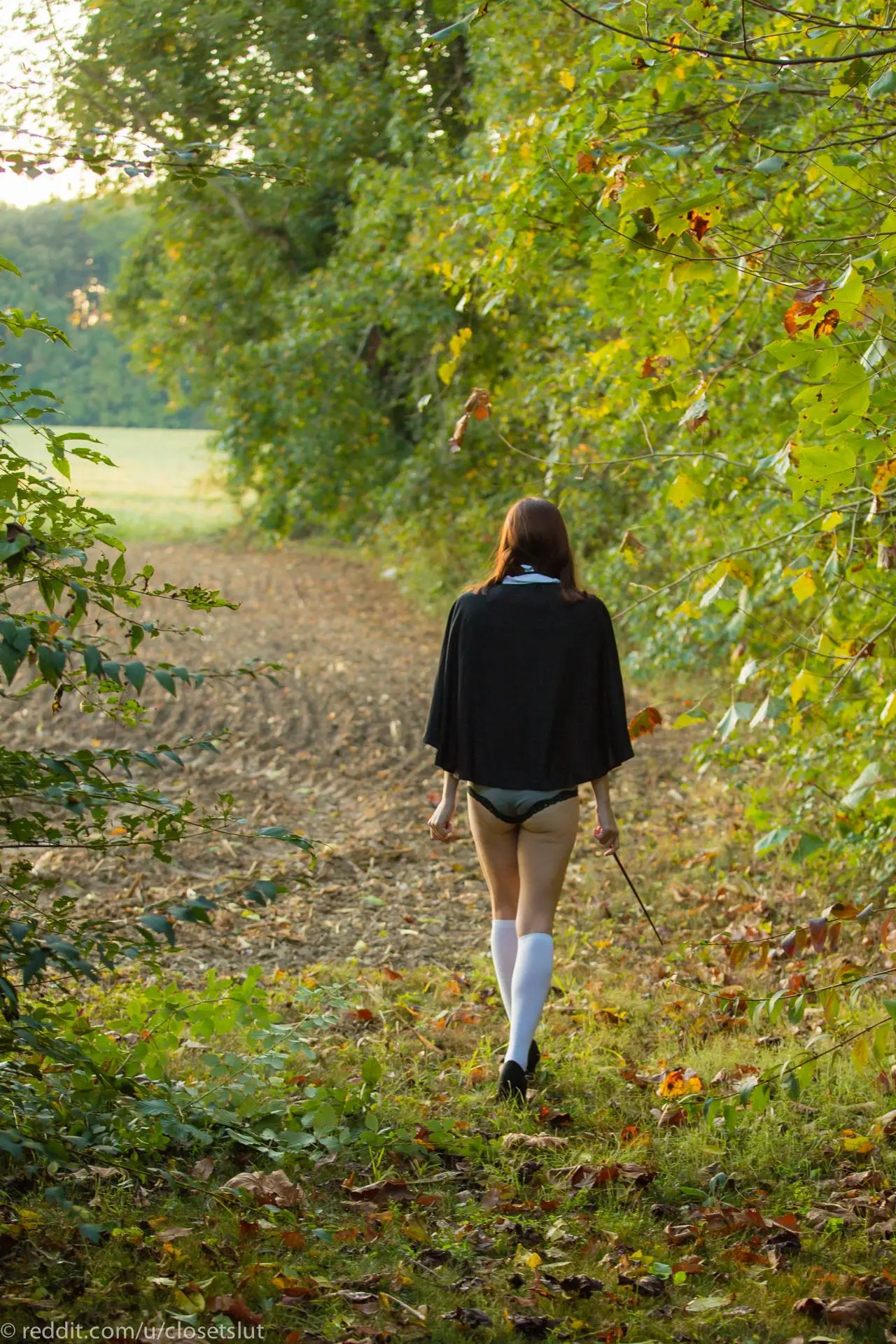 Hermione cosplay woman in a grey skirt and white thigh-high socks posing in a forest, showing her backside