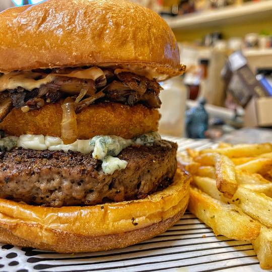 Impossible burger on a brioche bun with an onion ring, bleu cheese, mushrooms, caramelized onion, everything aioli and rosemary fries on the side.