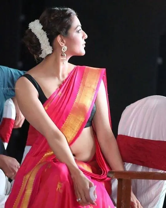 Kajal Aggarwal in a pink and gold saree with a black blouse, posing with a namaste greeting at an event.