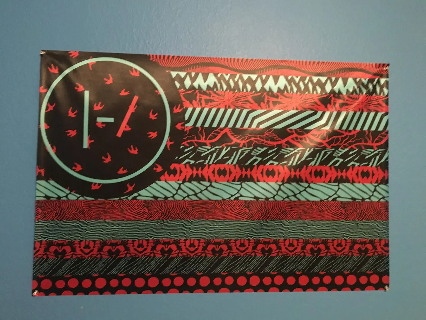 Twenty One Pilots flag with a circular emblem and colorful stripes hanging on a blue wall