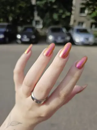 MOONCAT showing off long metallic pink and gold nails, a silver ring, and a fine line leaf tattoo on a fair wrist