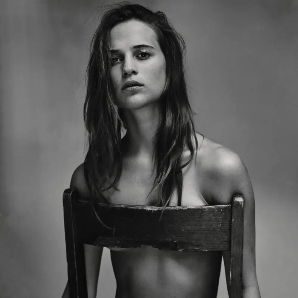 Alicia Vikander posing in a white suit, black dress, and floral gowns with a thigh tattoo