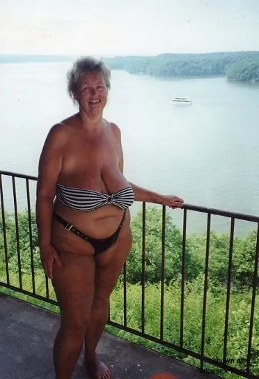 Saggy MILF with short blonde hair in a striped strapless bikini and tiny thong posing on a balcony