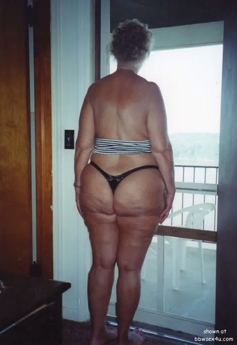 Saggy MILF with short blonde hair in a striped strapless bikini and tiny thong posing on a balcony