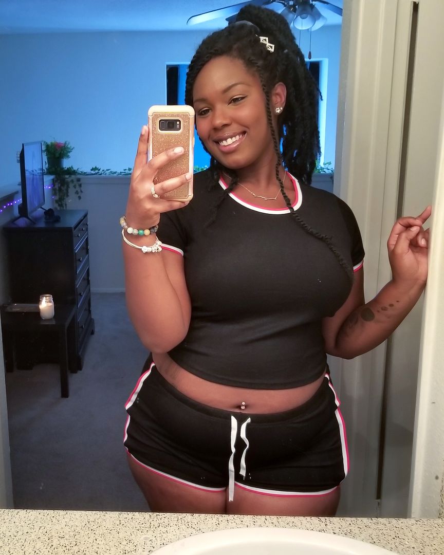 Curvy black woman with dreadlocks taking a mirror selfie in a black high waisted shorts set with red and white trim