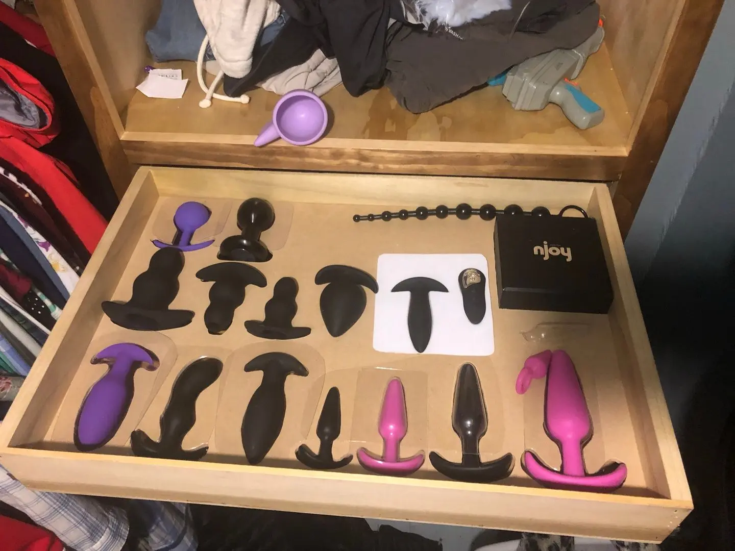 Sex toys including dildos, vibrators, and anal beads organized in a wooden dresser drawer