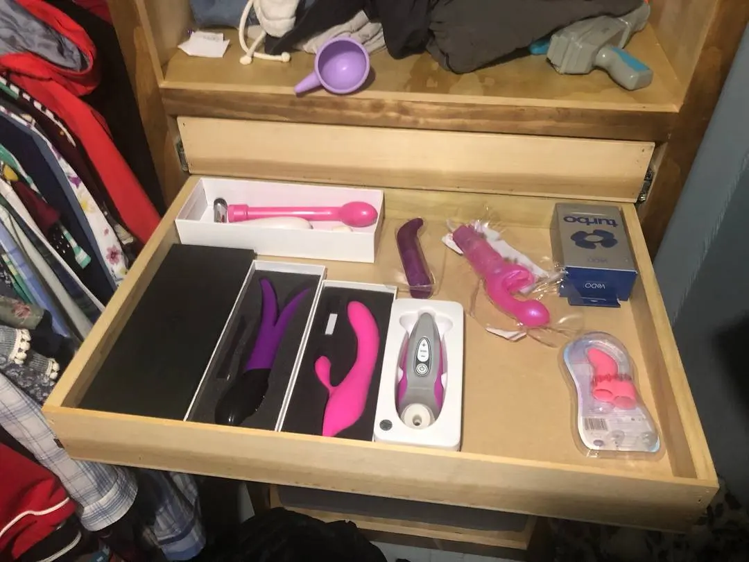 Sex toys including dildos, vibrators, and anal beads organized in a wooden dresser drawer