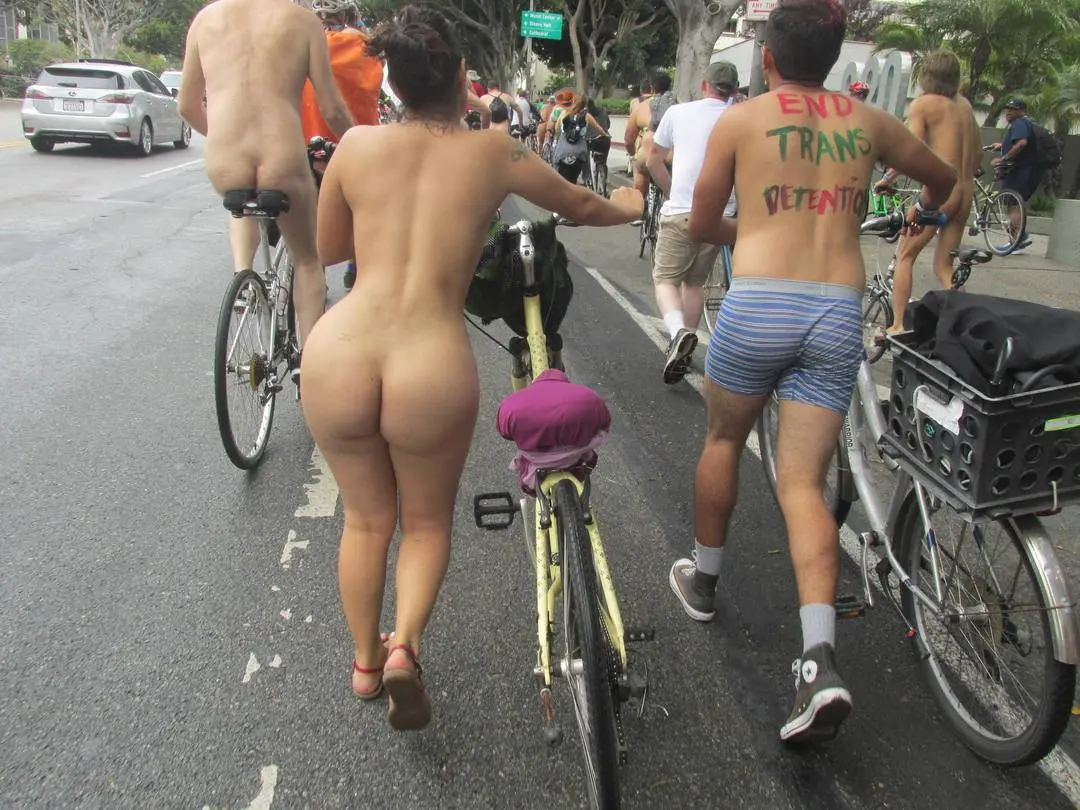 Thick latina with heart pasties and tattoos riding a bicycle at WNBR SF with an interracial group