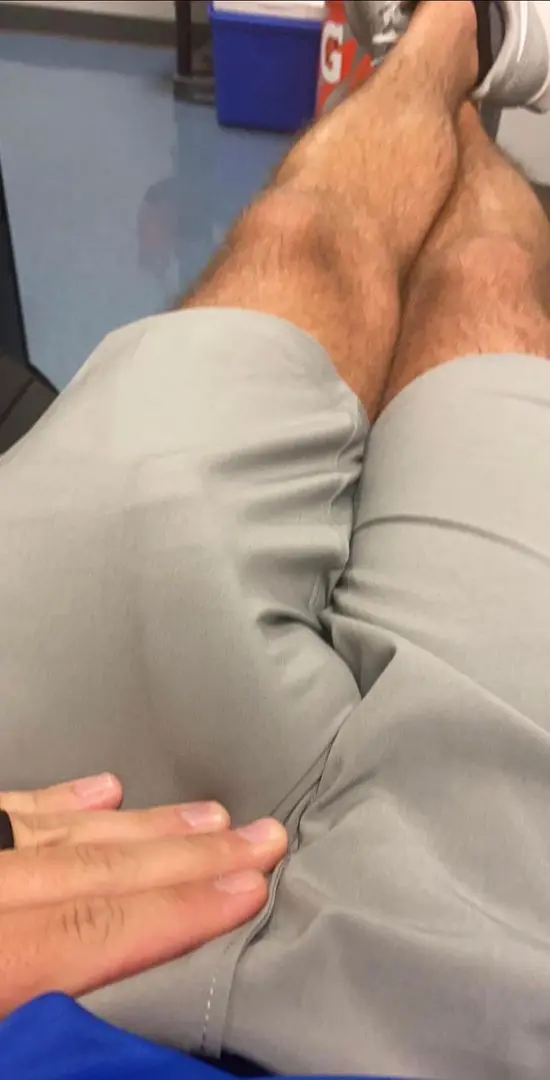 White athletic man in grey pants with a visible dick print and a hand resting on his thigh