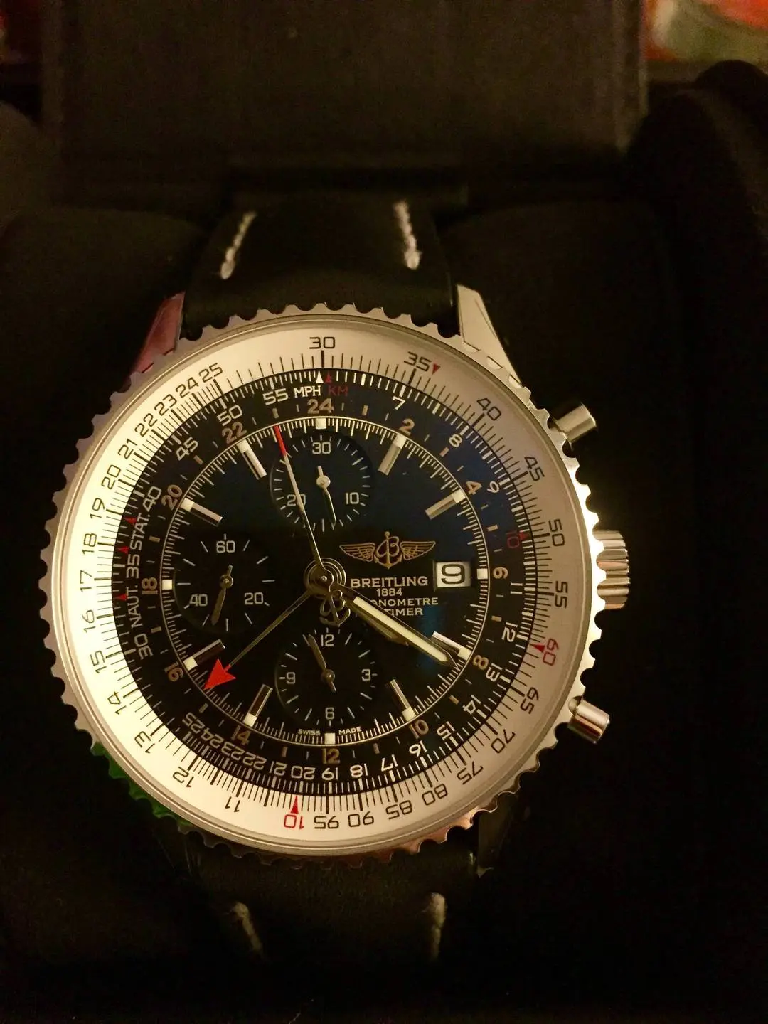 Close-up of a Breitling Navitimer World luxury watch with a black face and leather strap on a dark background