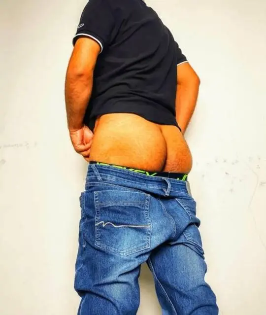 Indian desi man mooning, showing his ass in a selfshot against a white wall.