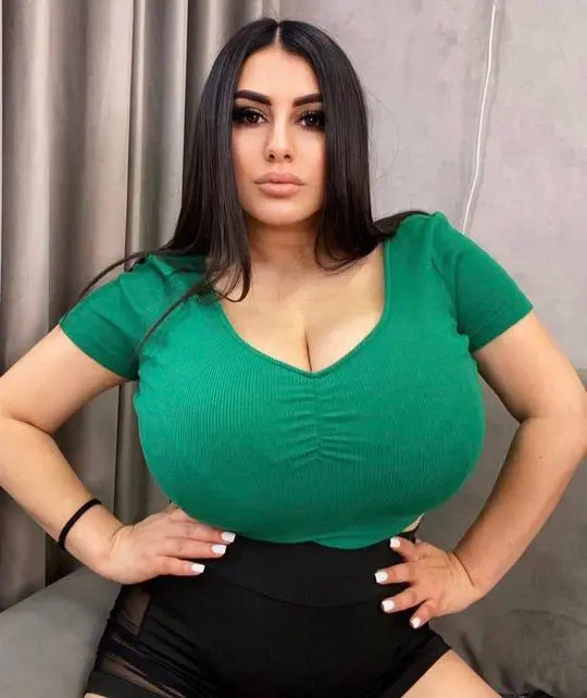 Curvy woman with long dark hair in a tight green ribbed top and black high-waisted shorts with mesh panels.