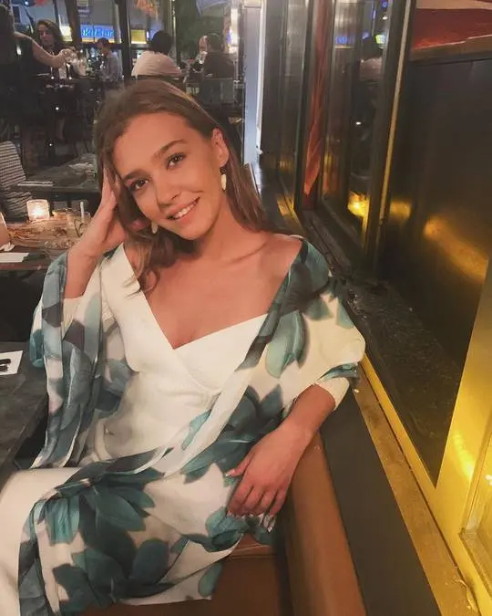 Melisa Döngel wearing a white off-the-shoulder summer dress and floral wrap at an outdoor restaurant