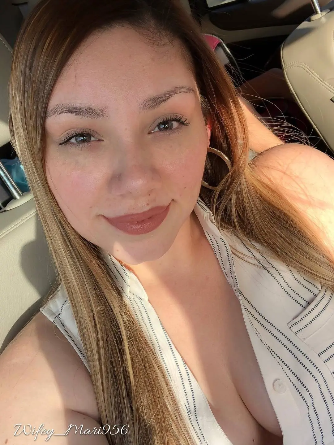Curvy latina Wifey_Mari956 in a white sleeveless shirt taking a smiling selfie in a car interior.