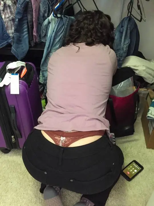 Sammi Starfish bending over in a pink t-shirt and black pants, showing a whaletail lace panty flash selfie