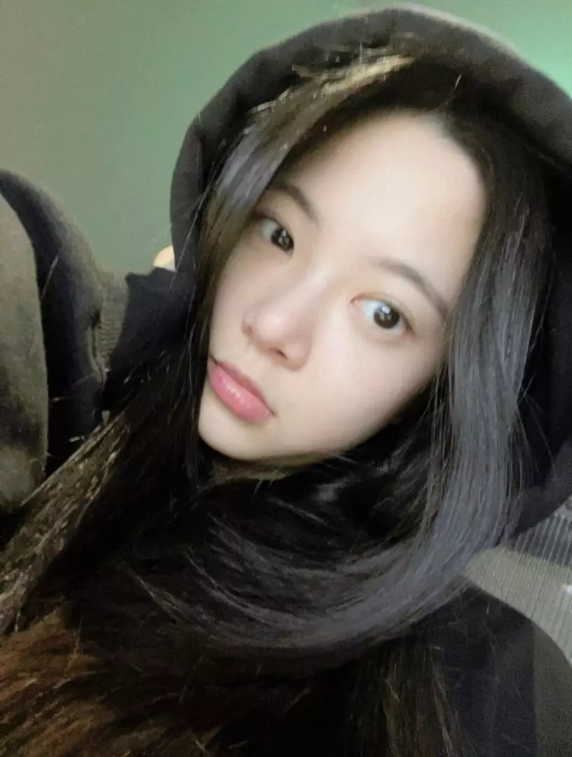 Hong Eunchae of LE SSERAFIM in a black hoodie selfie against a green wall