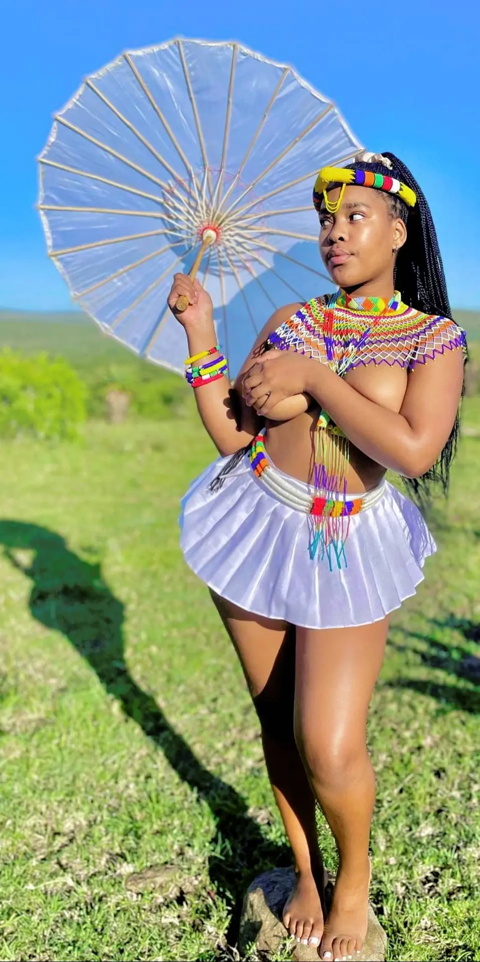 Beautiful Zulu Maiden in traditional beaded attire and white skirt posing topless with a clear umbrella