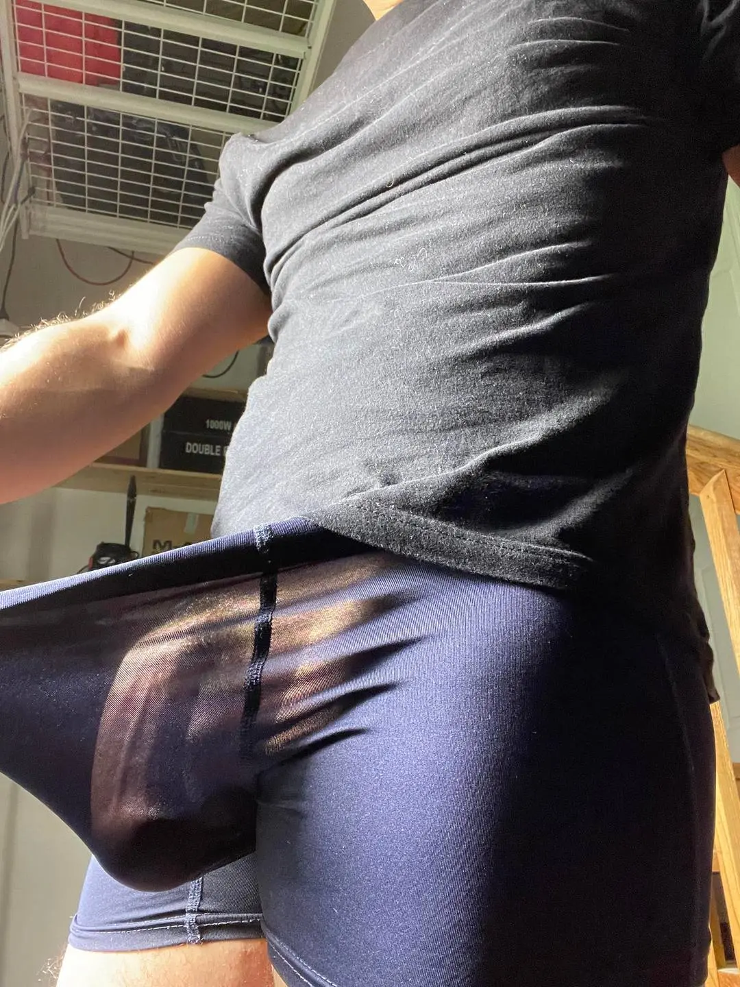 Athletic white man in a black t-shirt and sheer blue compression shorts showing a prominent cock outline.